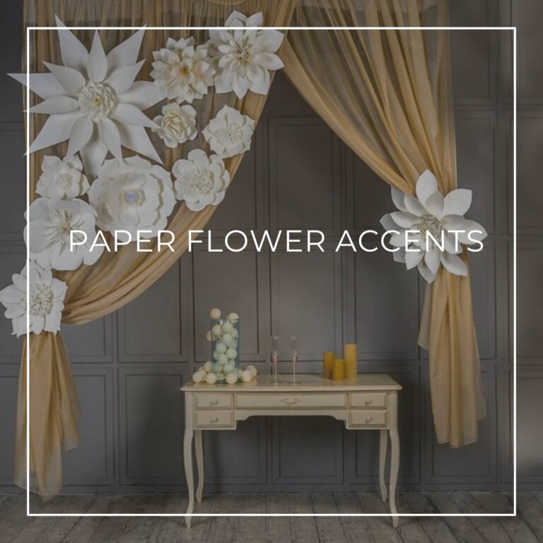 white paper flowers attached to sheer gold fabric swag curtain backdrop behind a console table