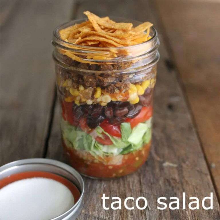 Layered taco salad mason jar with seasoned beef, black beans, corn, and tortilla strips, labeled “taco salad”