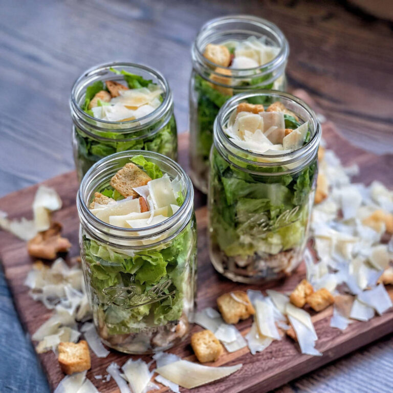 Caesar salad mason jars layered with romaine, croutons, and shaved parmesan on a wooden board