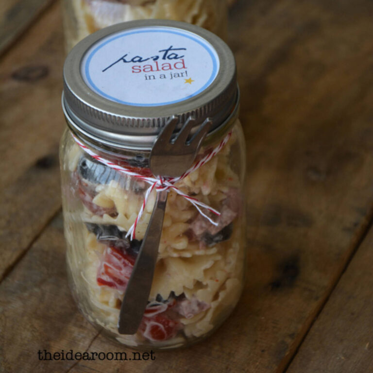 Close-up of a pasta salad mason jar with a “pasta salad in a jar” label and fork tied in red and white twine