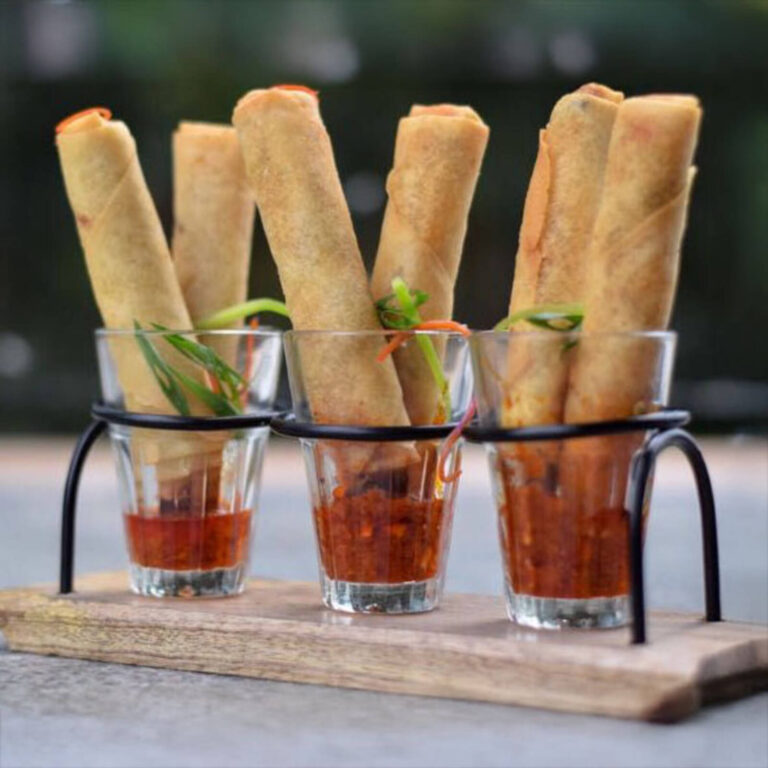 Crispy spring rolls standing in shot glasses of sweet chili sauce with scallion and carrot garnish