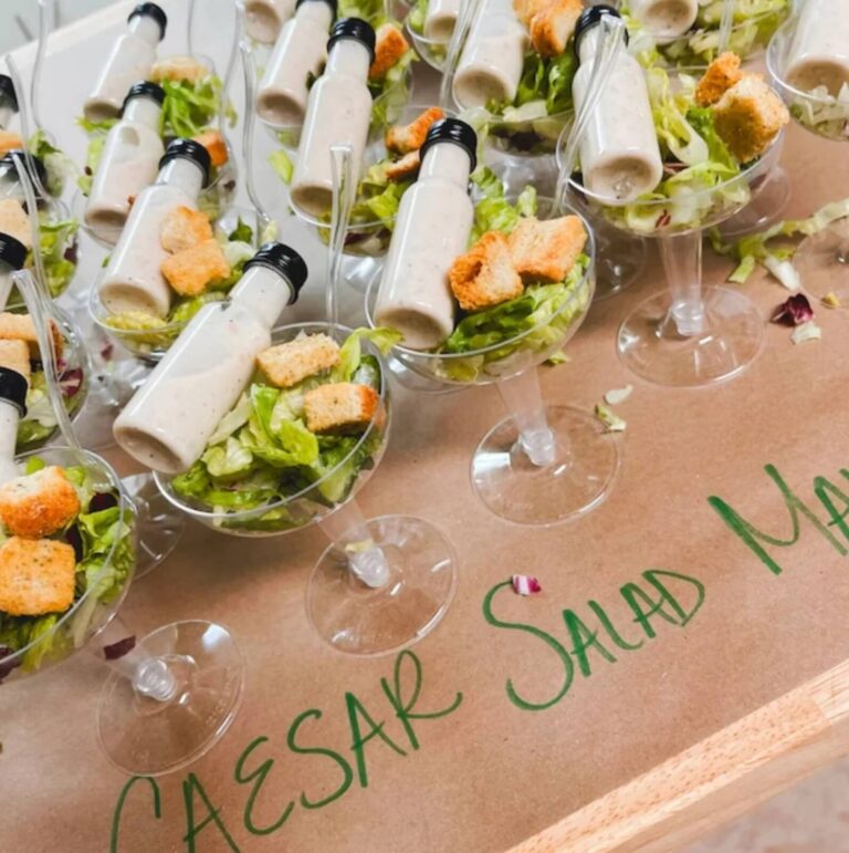 Caesar salad served in coupe glasses with mini dressing bottles tucked inside and a side of croutons