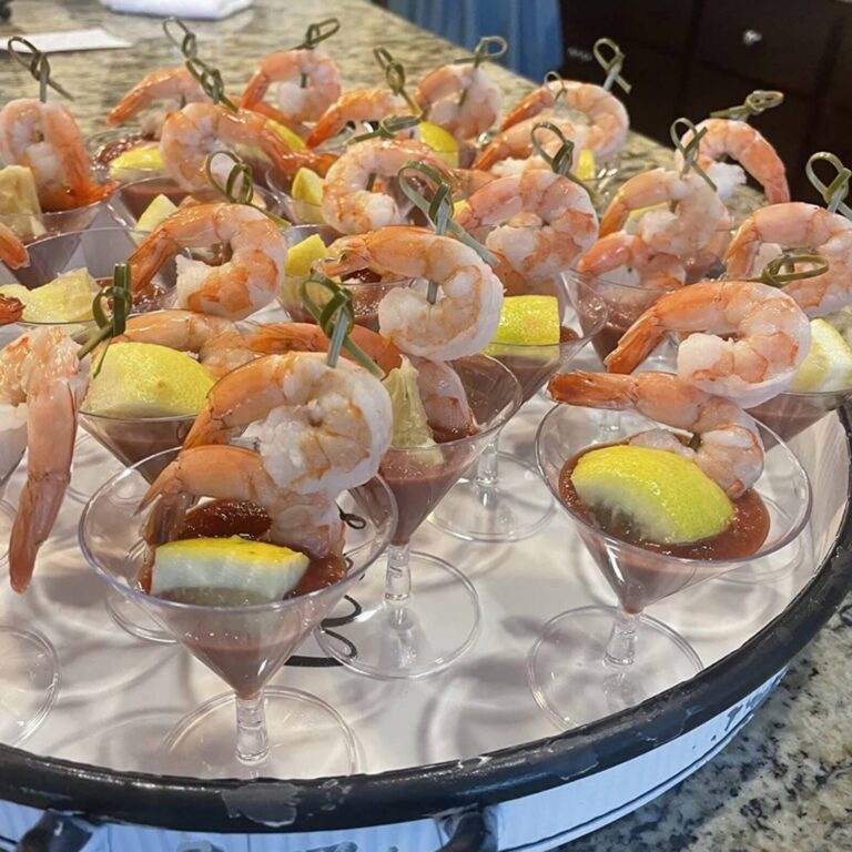 Shrimp cocktail platter with poached shrimp hooked over stemmed glass rims, cocktail sauce, and lemon wedges
