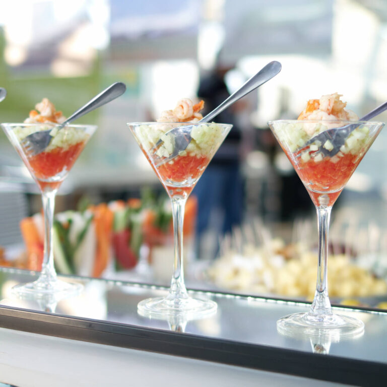 Shrimp cocktail in martini glasses with cocktail sauce, diced cucumber, and a poached shrimp garnish