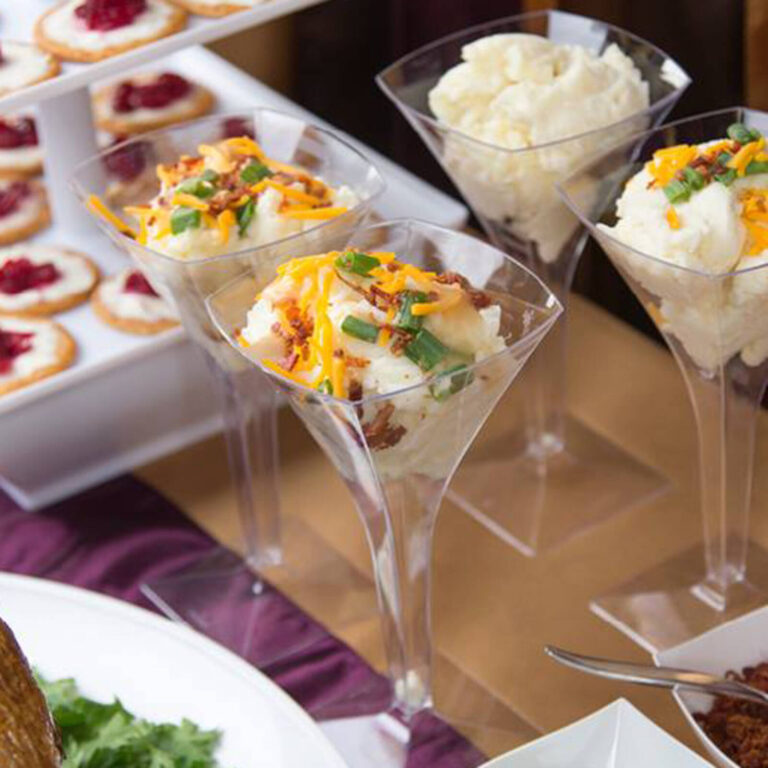 Mashed potato bar in martini glasses topped with shredded cheddar, bacon bits, and chives