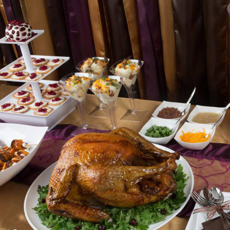 Mashed potato martini bar alongside a roast turkey, cranberry-topped crackers, and condiment bowls on a holiday buffet table