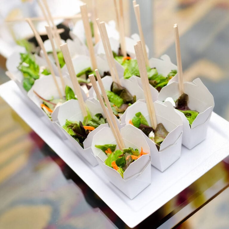 White takeout boxes filled with mixed greens salad and chopstick picks