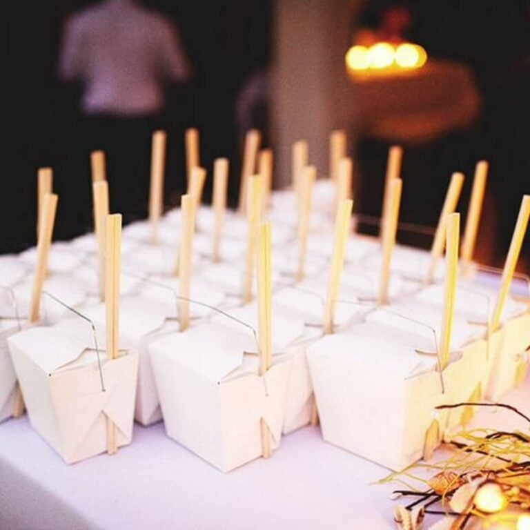 Rows of empty white takeout boxes with chopsticks styled at a dimly lit evening party