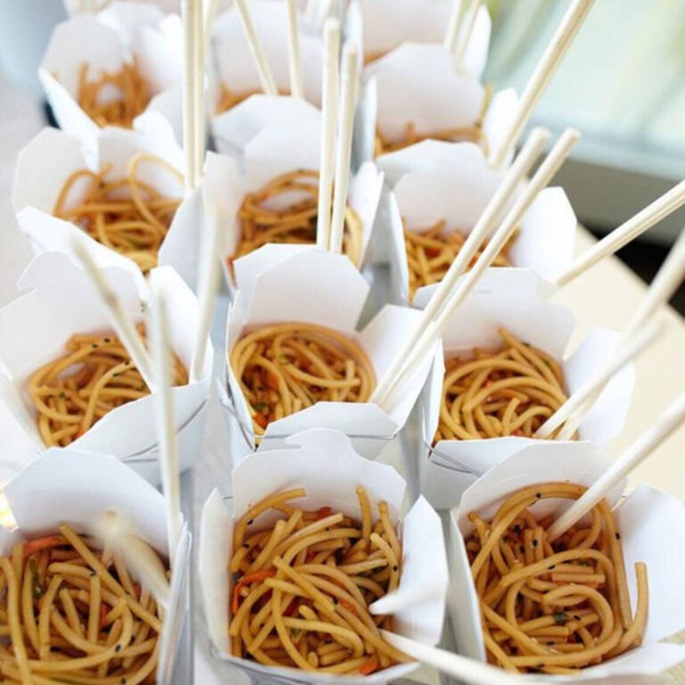 White takeout boxes filled with sesame lo mein noodles, close-up with multiple chopsticks