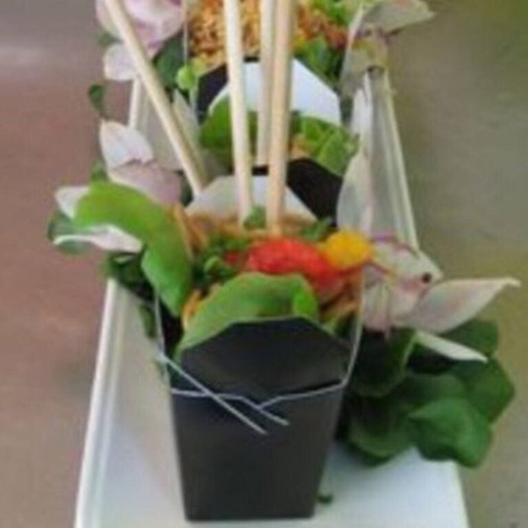 Takeout box filled with salad surrounded by a tropical leaf and flower garnish