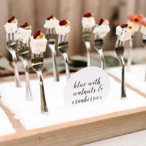 Blue cheese cubes with candied walnuts and cranberries on tasting forks in a snow-themed display labeled "blue with walnuts & cranberries"