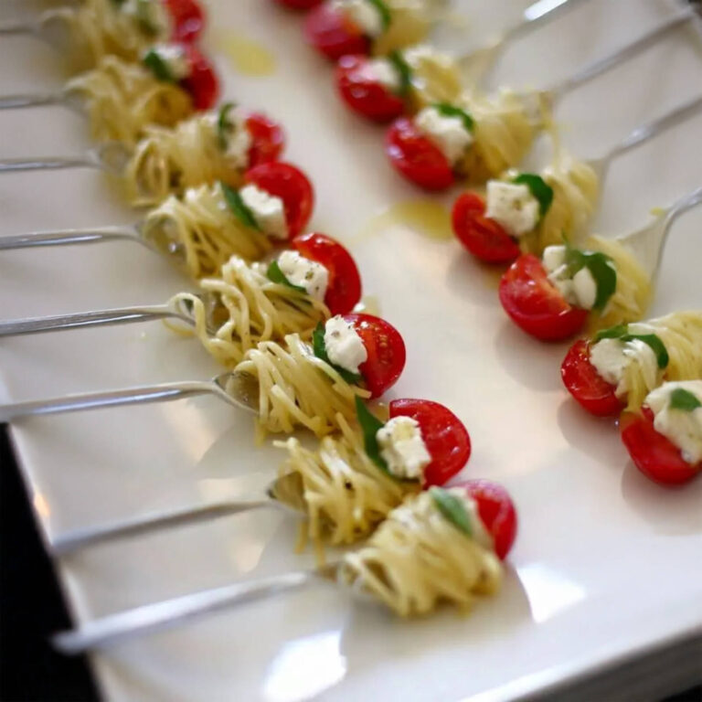 Pesto pasta nests with cherry tomato and mozzarella on silver tasting forks arranged in rows