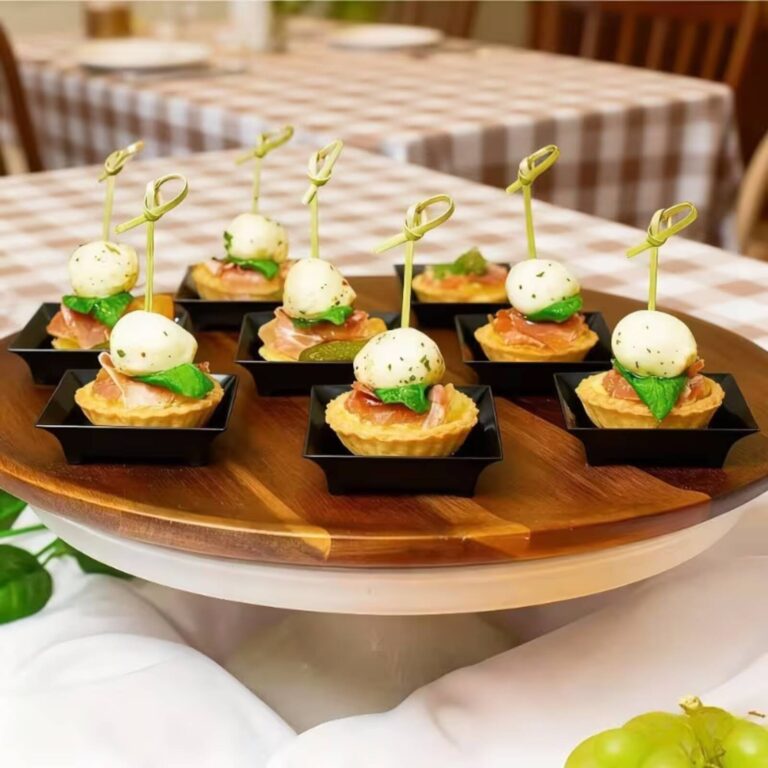 Prosciutto and mozzarella ball canapés with basil on black square tasting plates arranged on a wooden board
