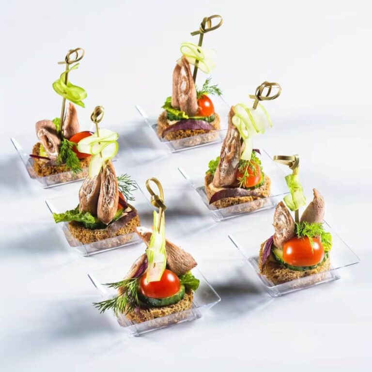 Smoked fish canapés with cucumber ribbon and cherry tomato garnish on clear square tasting plates with gold knot picks