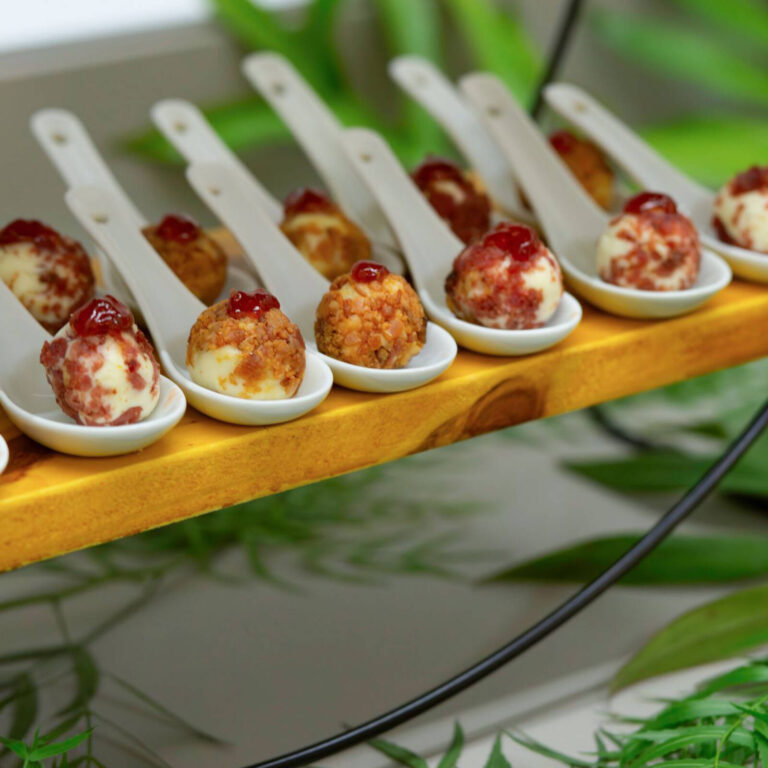 Cream cheese bites topped with bacon and raspberry preserve served on white tasting spoons