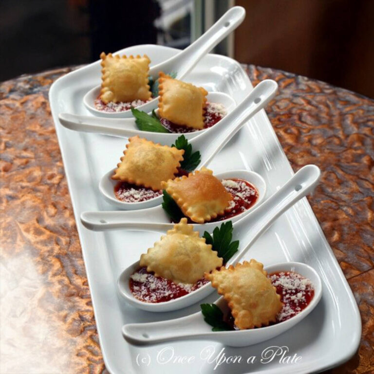 Fried ravioli bites in marinara sauce with parmesan served on white tasting spoons