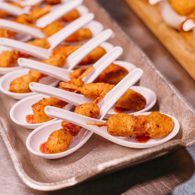 Breaded nugget bites with hot sauce drizzle served on white tasting spoons