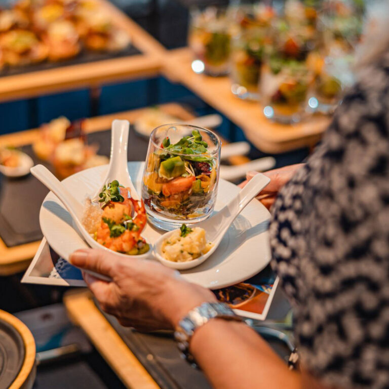 Assorted tasting spoon bites including shrimp, verrine salad, and risotto on a plate held by a guest