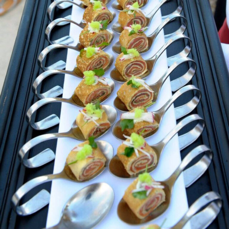 Smoked salmon pinwheel rolls with radish and herb garnish on silver tasting spoons