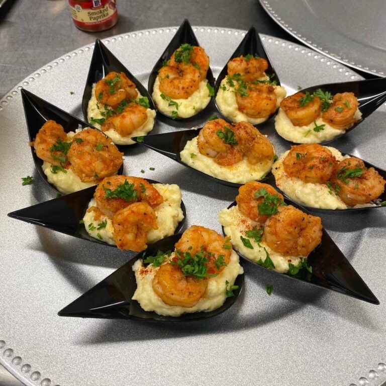 Shrimp and grits bites served on black teardrop tasting spoons with parsley garnish