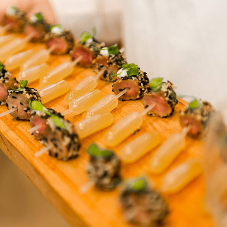 Sesame-crusted seared beef bites with citrus sauce pipettes and microgreens on a wooden board
