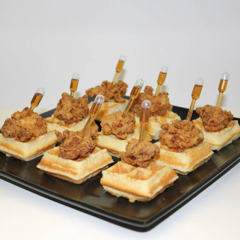 Mini chicken and waffle bites with honey sauce pipettes on a black tray