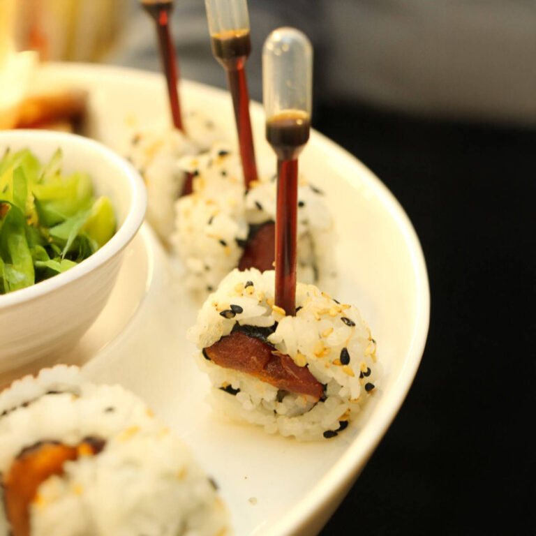 Sesame sushi rice balls with tuna filling and soy sauce pipettes on a white plate with pickled ginger