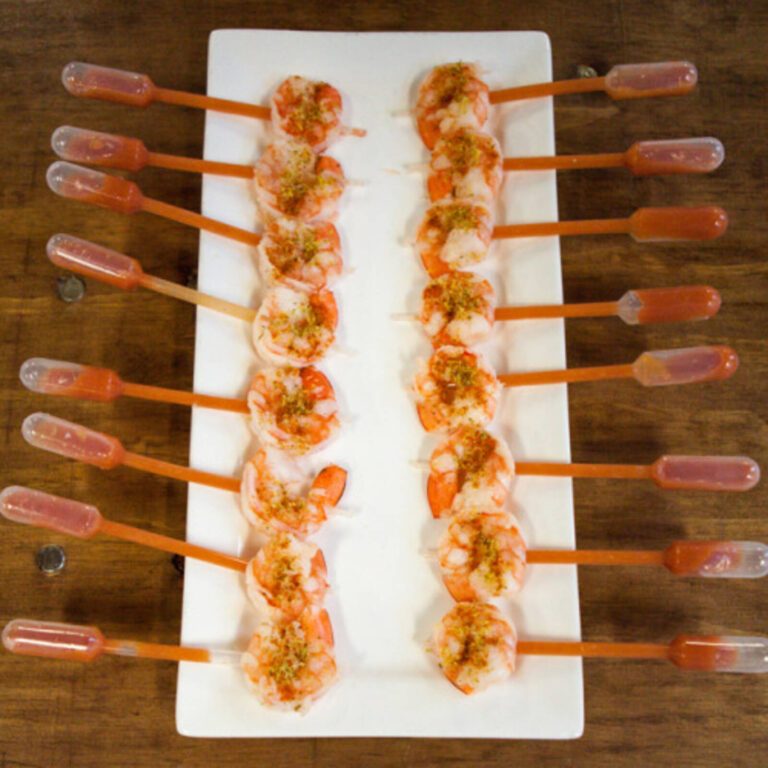 Grilled shrimp skewers with citrus sauce pipettes arranged in rows on a white platter