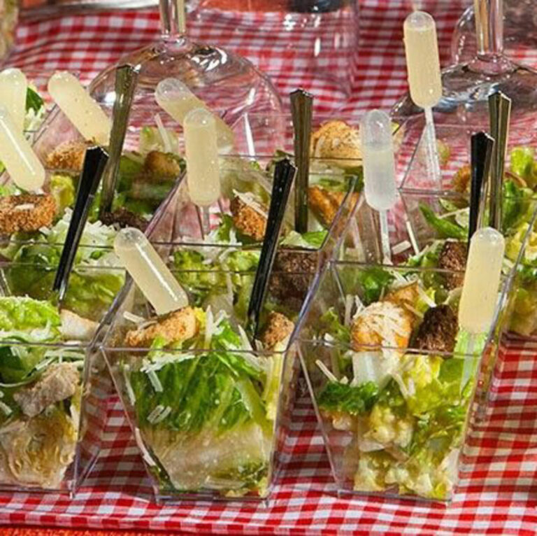 Caesar salad cups with dressing pipettes, croutons, and parmesan on a red checkered tablecloth