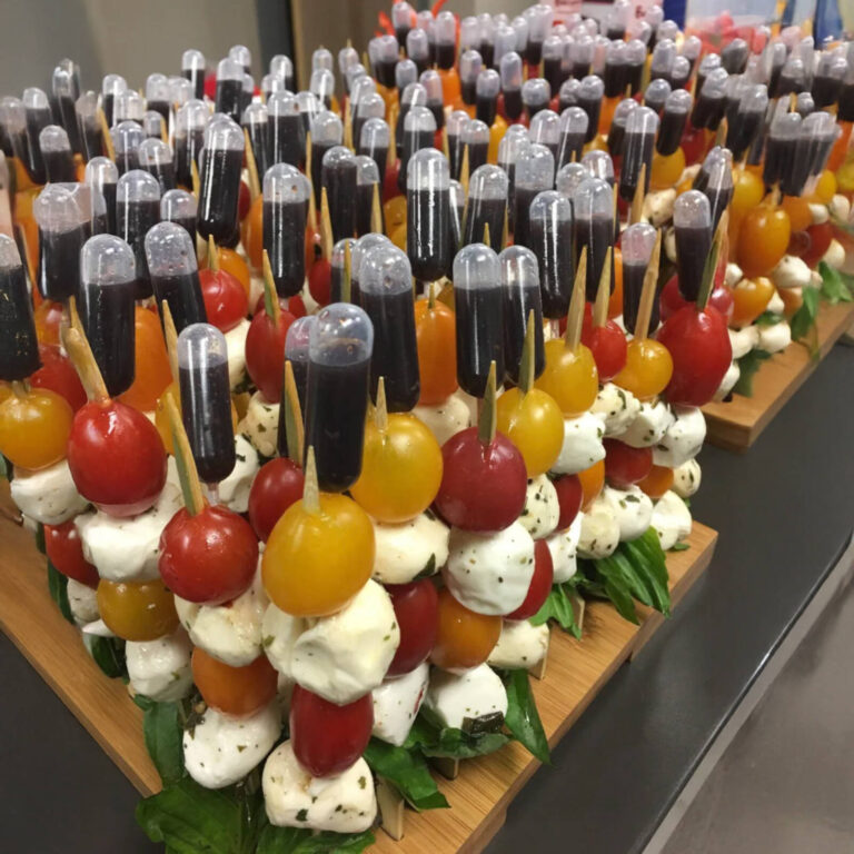 Caprese skewers with cherry tomatoes, mozzarella, and balsamic sauce pipettes displayed in large catering rows