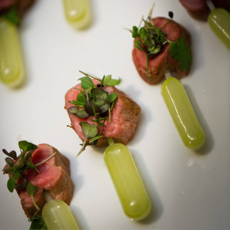Seared beef bites with wasabi sauce pipettes and microgreens on a white plate