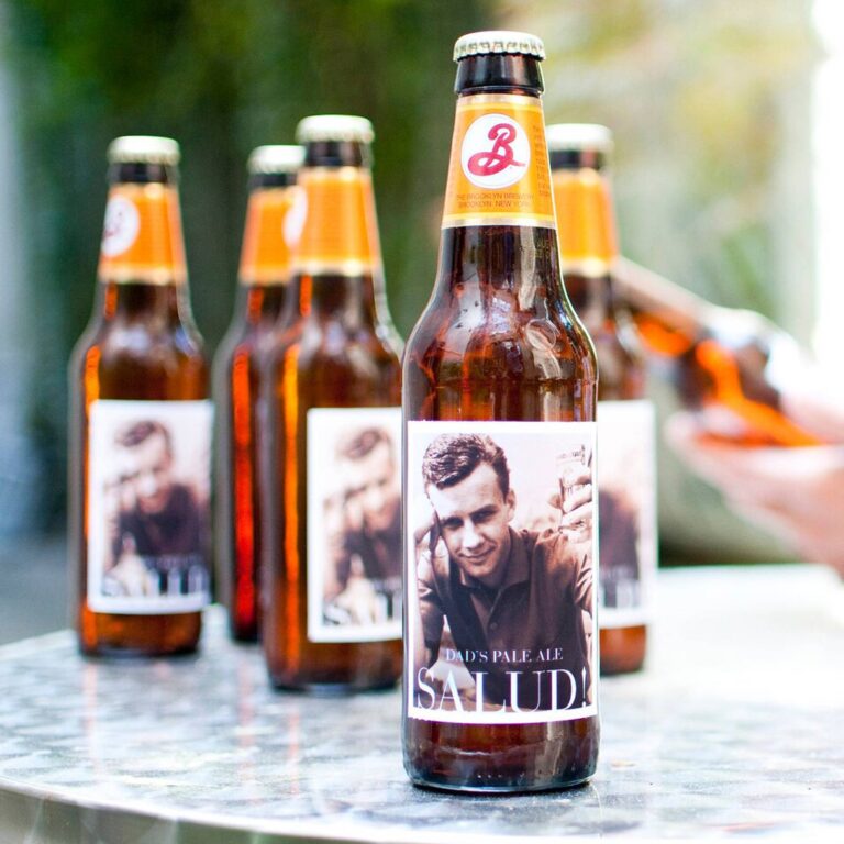 Row of Brooklyn Brewery bottles with "Dad's Pale Ale, Salud!" labels featuring a sepia-toned photo of a man raising a glass