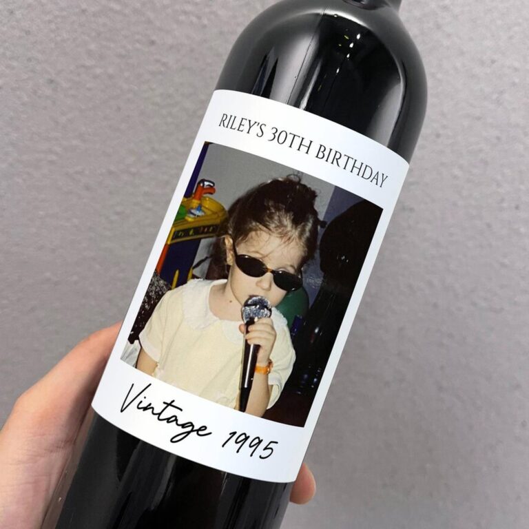 Wine bottle with a “Riley's 30th Birthday” label featuring a childhood photo of a girl in sunglasses singing into a toy microphone, “Vintage 1995”