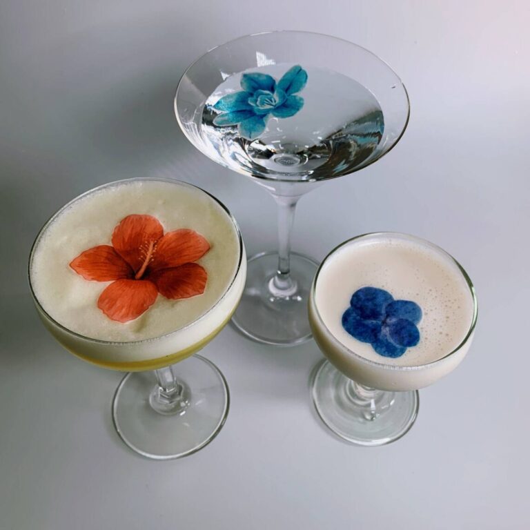 Edible hibiscus, orchid, and pansy toppers on three foam-topped and clear cocktails
