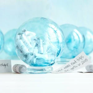 Bright blue glass wishing ball filled with rolled paper wishes, unedited product photo