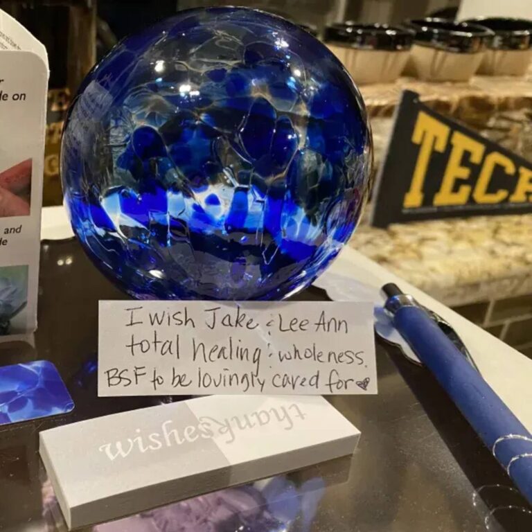 Blue glass wishing ball beside a handwritten wish note reading I wish Jake and Lee Ann total healing