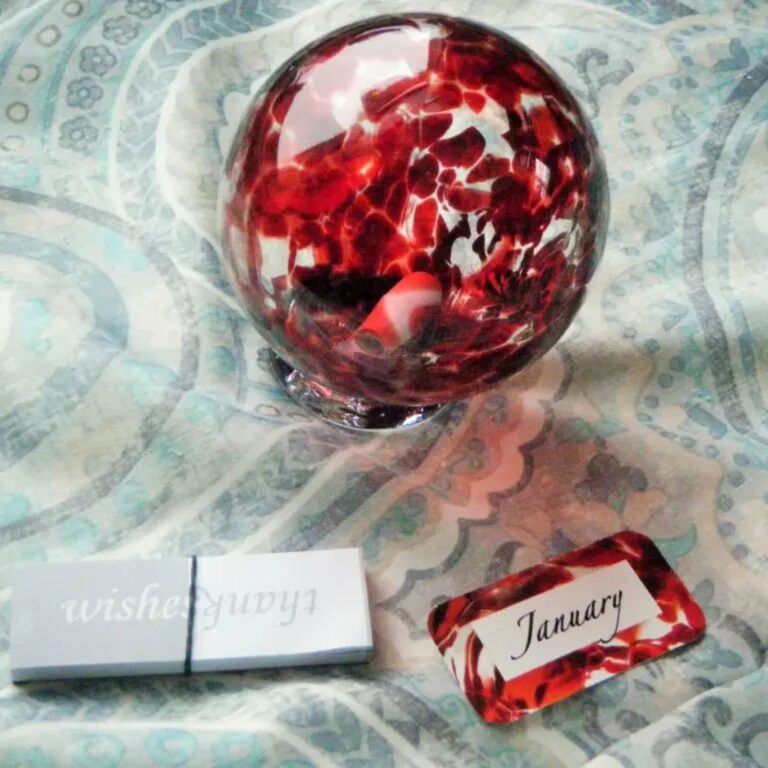 Deep red glass wishing ball with a handwritten January date card beside it